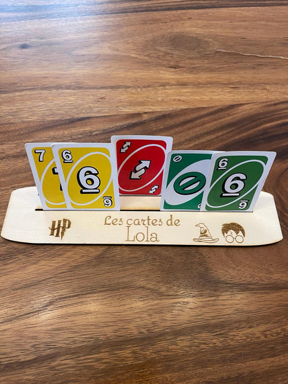 Personalized wooden card holder with engraved name and Harry Potter motifs holding colorful playing cards on a wooden table.